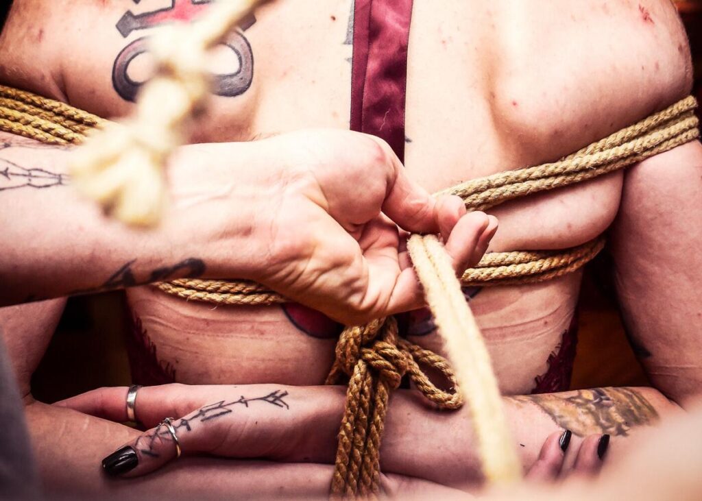 The tattooed back of someone as they are being tied up